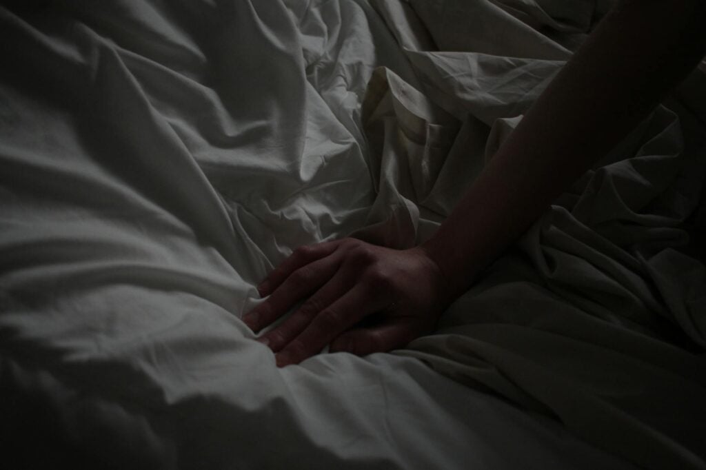 A close-up of a hand resting on white sheets, creating a sense of calm.