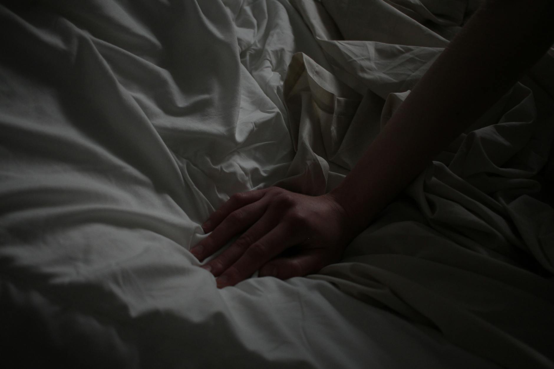 A close-up of a hand resting on white sheets, creating a sense of calm.