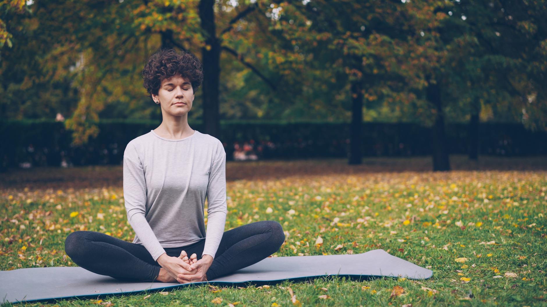 A woman practices yoga in a peaceful outdoor park setting during fall.
