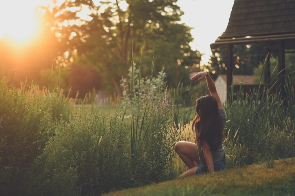 How Can I Manage Persistent Sadness That Doesn’t Go Away? 1 A woman sitting in a garden, stretching her arm under the warm sunset light, embracing nature's tranquility.