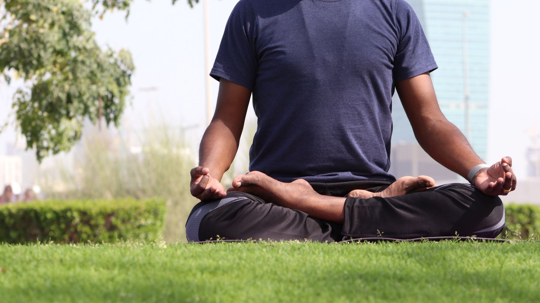 A man practicing meditation in lotus pose on a sunny day in an outdoor urban park.