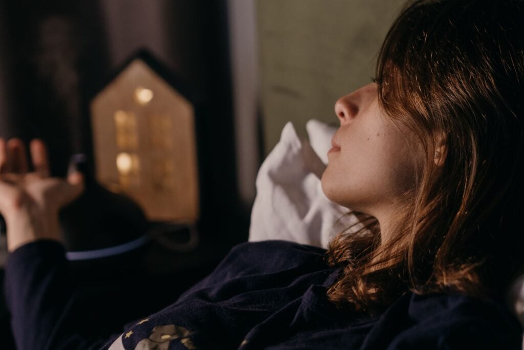 A serene woman lies in bed under soft lighting, creating a peaceful indoor ambiance at night.