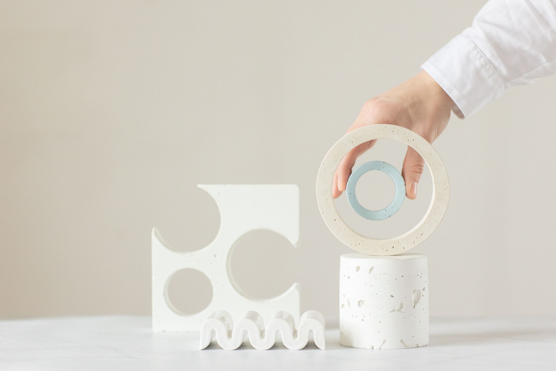 A hand arranging minimalist geometric shapes in a bright indoor setting.