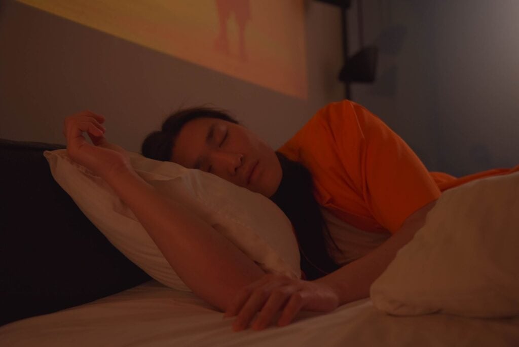 A sleeping Asian man in a bed, enveloped in a moody atmosphere with soft lighting.