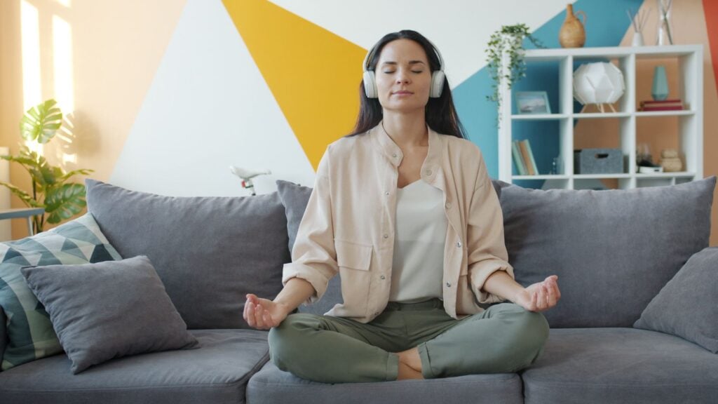 How Can I Manage Mental Health-Related Decision Fatigue and Improve Daily Functioning? 2 Woman in serene meditation pose with headphones on a stylish couch indoors.