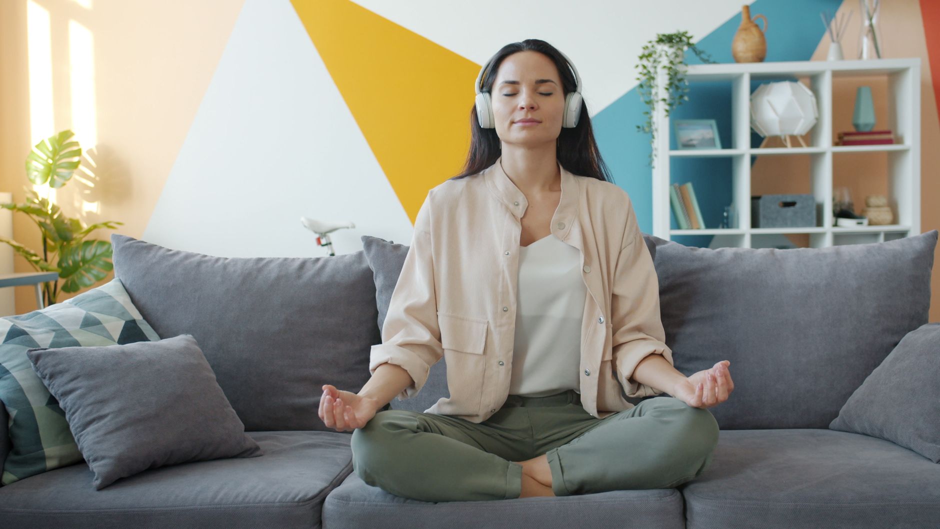 Blog 2 Woman in serene meditation pose with headphones on a stylish couch indoors.